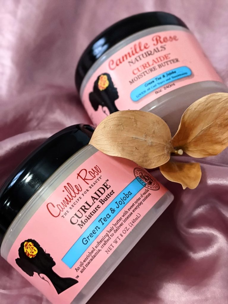 October haul for natural hair. Two containers of Camille Rose Naturals Curlaide Moisture Butter photographed on a pink silk fabric with a yellow leave/branch in between Camille Rose Naturals Curlaide Moisture Butter