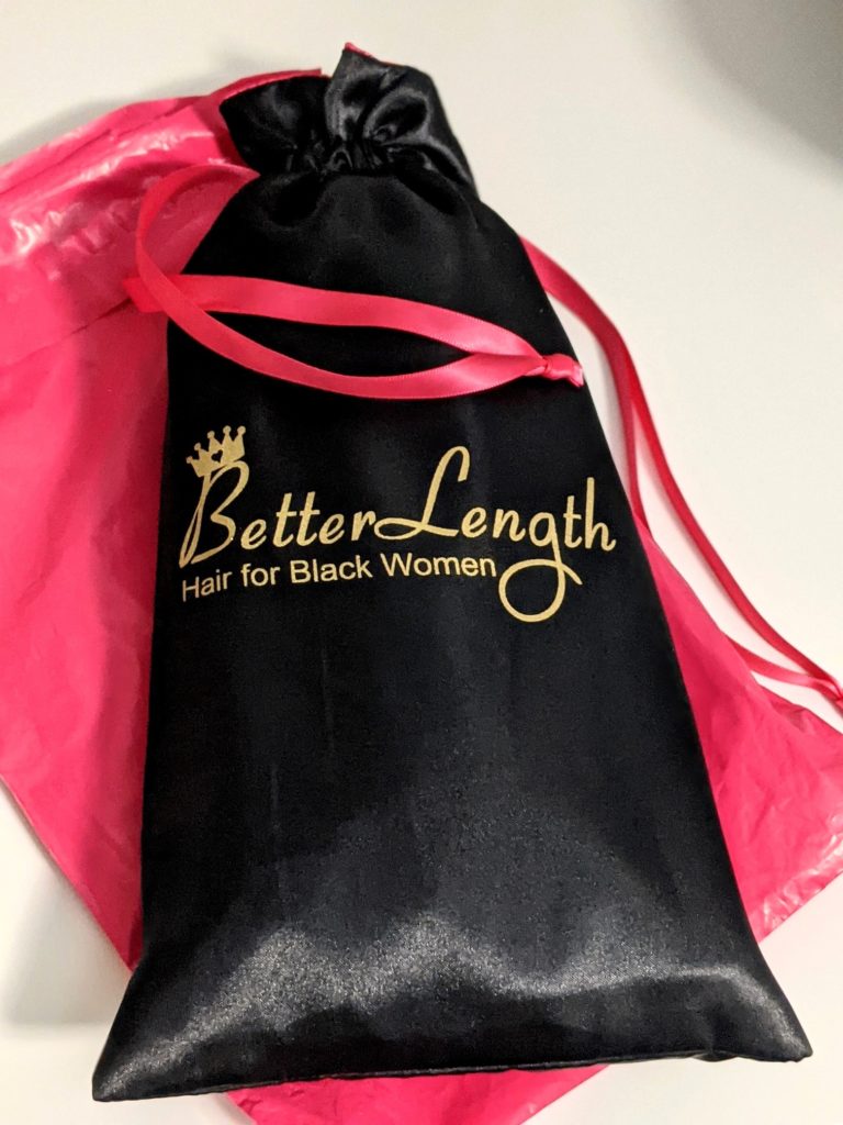 “BetterLength Hair for Black Women” label in gold typography dusted with some shimmer on a gorgeous black satin drawstring bag, lined with hot pink on the inside and on the drawstring